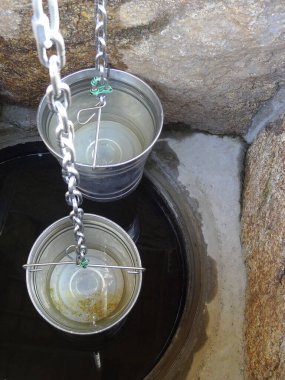 Metal kovalar, berrak suyun üzerinde taş kuyunun içinde asılı.