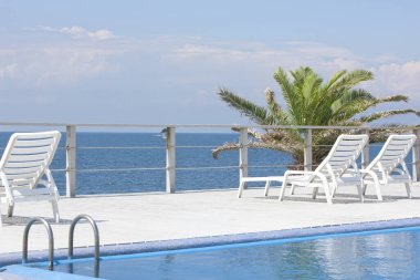 Güneş yatakları ve mavi deniz manzaralı boş yüzme havuzu alanı 