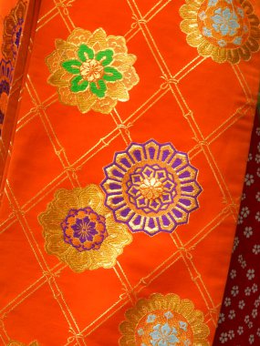 Parlak turuncu kumaş. Karmaşık altın çiçek desenleri var.