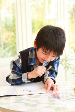 Asyalı çocuk kağıda resim çiziyor.