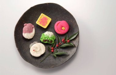 Siyah seramik tabağa dizilmiş renkli geleneksel Japon tatlıları.