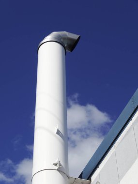 Endüstriyel binanın çatısına uzanan uzun beyaz metal baca.