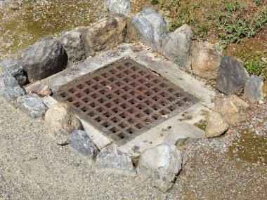 Metal rögar ızgarası. Etrafı büyük kaba taşlarla çevrili.