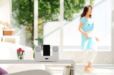 Parlak odada modern hoparlörün yanında yürüyen kadın.