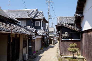 Mavi gökyüzünün altındaki geleneksel Japon ahşap evleri arasında dar bir sokak.