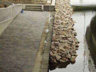 Durgun suyun yanındaki taş yol gökyüzünü ve kayaları yansıtıyor.