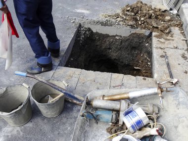 Alet ve kovalarla deliğin yanında duran işçiler