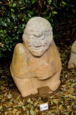 Yeşil yapraklar arasında çömelmiş şekilleri tasvir eden yıpranmış taş heykel