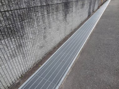 Dışarıdaki beton duvarın yanında çalışan uzun metal drenaj ızgarası.