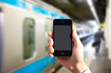 Bulanık tren istasyonu arka planında elinde akıllı telefonu olan birinin görüntüsü.