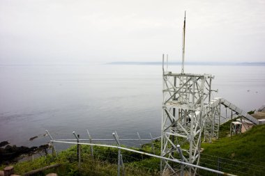 Çimenli kıyı şeridi yakınlarındaki sakin denize bakan metal gözlem kulesi.