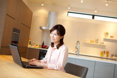 Güzel genç Asyalı kadın evde dizüstü bilgisayar kullanıyor.       