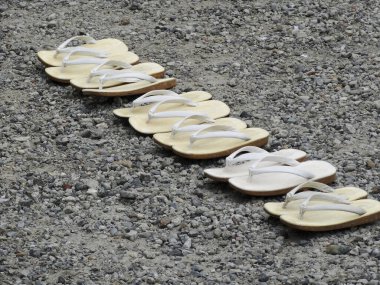 Sahildeki parmak arası terliklerin yakın çekimi, gri çakıl taşlarının sandaletleri.