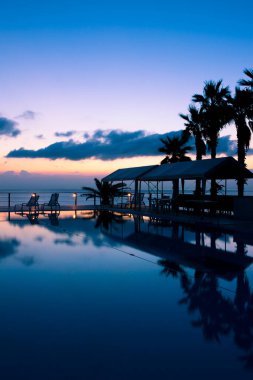 Gün batımında sandalyeli ve palmiye ağaçlı bir havuz