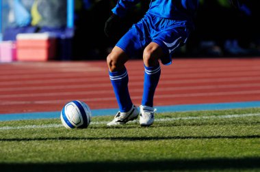 Bir futbolcu sahada futbol topunu tekmeliyor.