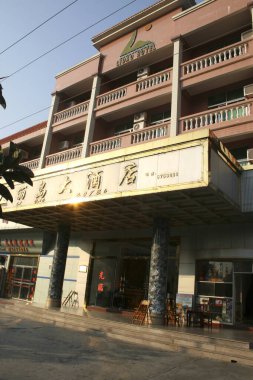 Güneşli otel binasının dış tarafında balkonlar ve büyük giriş işareti var.