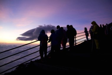 İzleyiciler, akşam gökyüzünde bir dağ manzarasından nefes kesen gün batımının keyfini çıkarıyorlar.