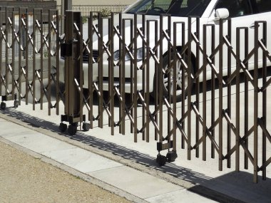 Kaldırımda park etmiş beyaz arabanın yanında metal kapı açılıyor.