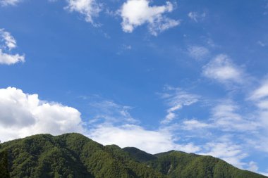 Gökyüzünde yeşil ağaçlar ve bulutlar olan güzel dağ manzarası       