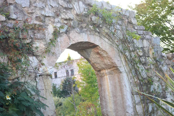a stone arch with a stone wall and trees