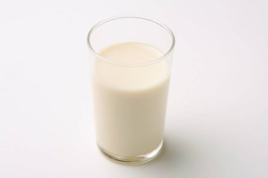 Temiz, açık renkli bir yüzeye asgari düzeyde yerleştirilmiş bir bardak taze süt.
