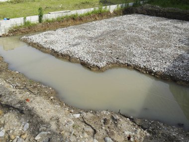 Kazılmış inşaat alanı çakıl vakfının yanında su birikintisi gösteriyor.