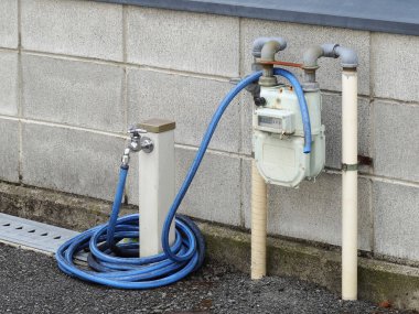 Su sayacı beton duvardaki mavi hortuma bağlı.