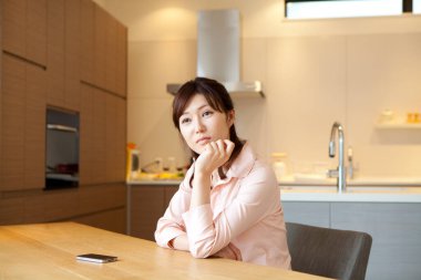 Güzel genç Asyalı kadın mutfakta telefonla masada oturuyor.