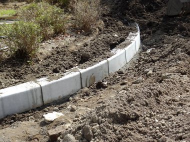 Eğri beton bloklar açık havada gevşek toprak arasında bahçe sınırı oluşturuyor.