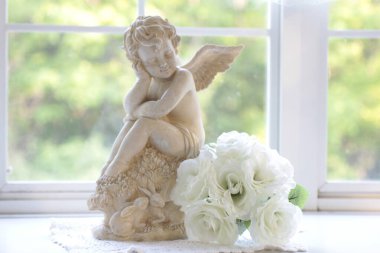 güzel küçük bir melek heykeli ve beyaz çiçekler pencere eşiğinde, antika bir ev dekorasyonu. 
