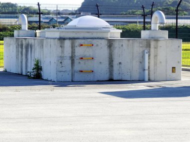 Çimlerle çevrili beton yapı ve güneş ışığı altında eskrim