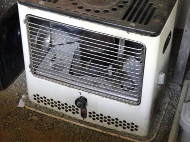 İçerideki tozlu beton zeminde duran eski metal ısıtıcı.