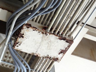 Elektrik kablolarıyla çevrili paslı metal bağlantı kutusu.