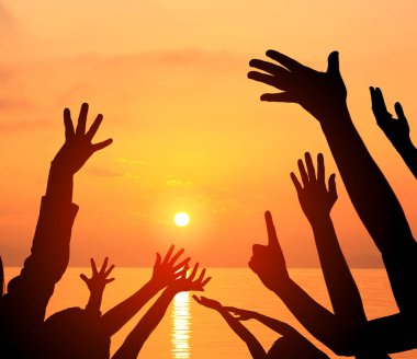 Siluetli eller parlak turuncu günbatımı gökyüzüne uzanıyor