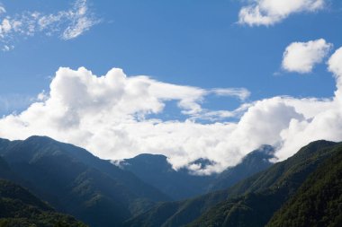 Gökyüzünde yeşil ağaçlar ve bulutlar olan güzel dağ manzarası       