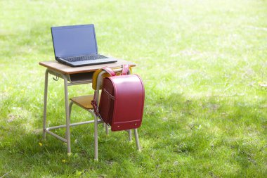 Yeşil çimlerin üzerinde bir koltuk ve okul çantası olan bir laptop.