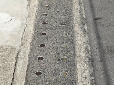Concrete sidewalk featuring multiple circular holes along surface