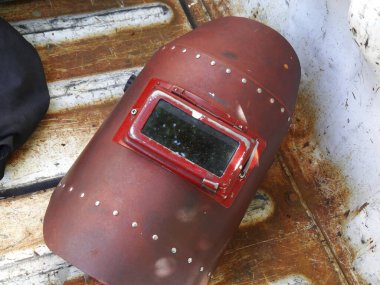 Paslı metal yüzeyde duran eski kaynak miğferi.