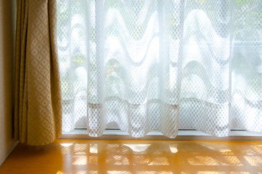 Güneş ışığı beyaz perdelerin arasından ahşap zemine doğru akıyor.