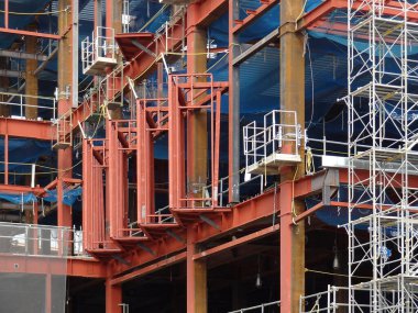 İnşaat alanında inşaat iskelesini destekleyen kırmızı çelik kirişler.