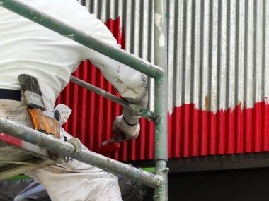 İşçi boyanmış metal duvar fırça kullanarak parlak kırmızıya boyanmış.