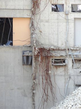 Kısmen yıkılan beton bina duvarından sallanan açıkta duran inşaat demiri.