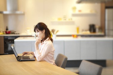 Güzel genç Asyalı kadın evde dizüstü bilgisayar kullanıyor.       