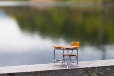 Oyuncak boş okul masası ve göl kenarındaki ahşap tahta üzerinde sandalye çimenlerin üzerindeki minyatür nesneler.