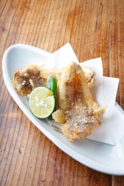 Tahta masada beyaz tabakta limonlu kızarmış balık.