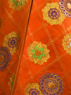 Altın çiçekli ve geometrik desenli canlı turuncu kumaş.