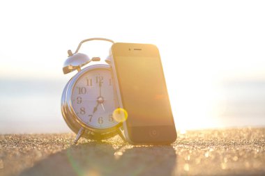 Gün batımında kumsalda çalar saatin ve akıllı telefonun yakın görüntüsü          