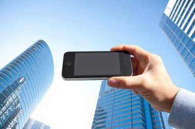 Mavi gökyüzü arka planında boş ekranlı akıllı telefonu tutan kişinin kırpılmış görüntüsü