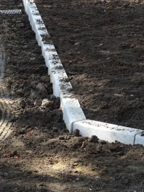 Koyu toprak bahçe yatağını çevreleyen beton kaldırımlar.