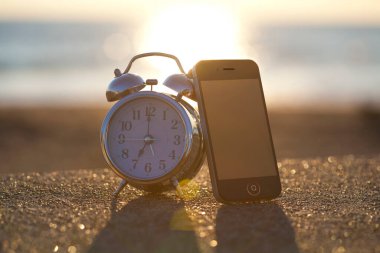 Gün batımında kumsalda çalar saatin ve akıllı telefonun yakın görüntüsü          